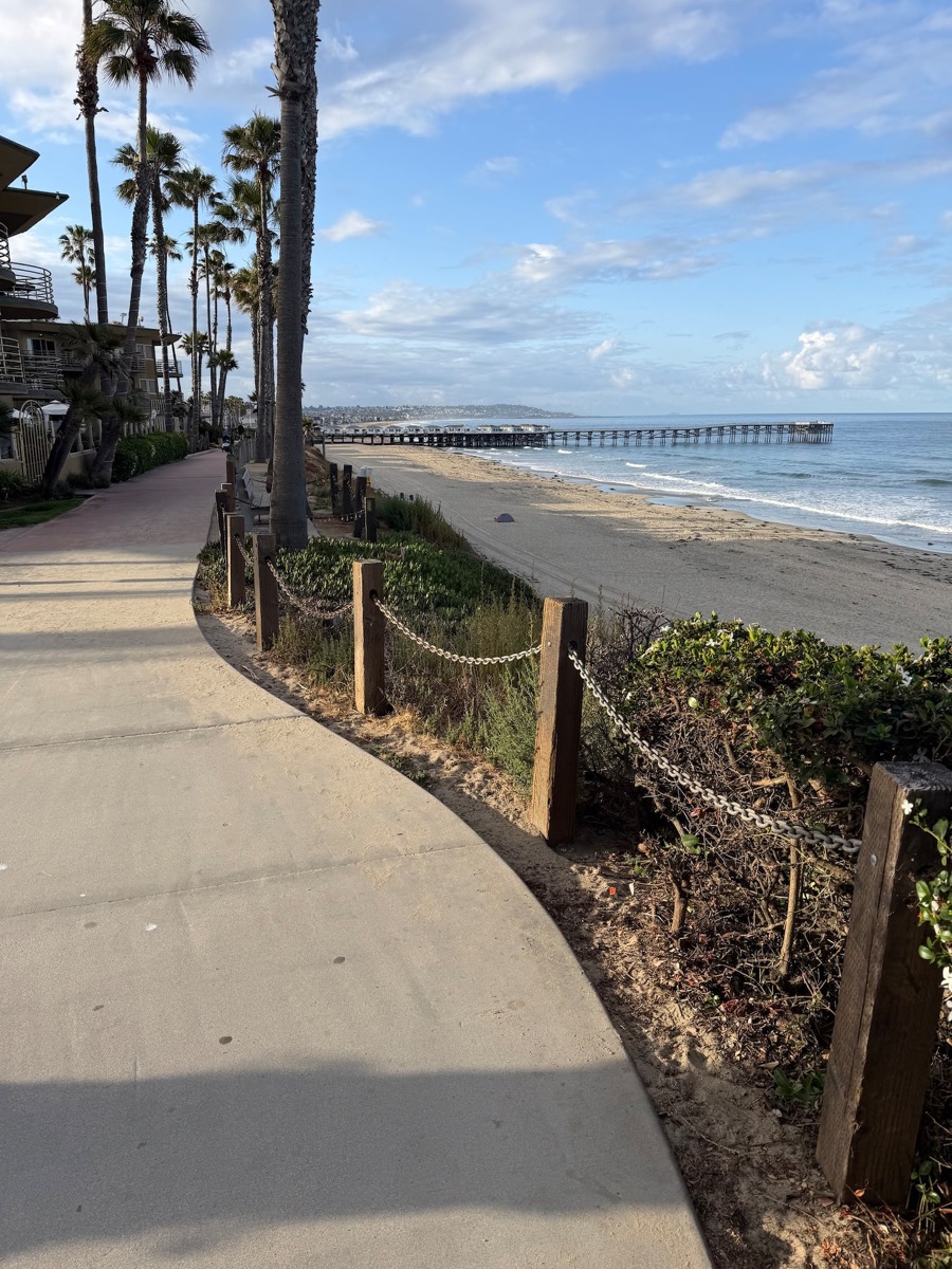 The paved boardwalk path running along the beach toward the pier