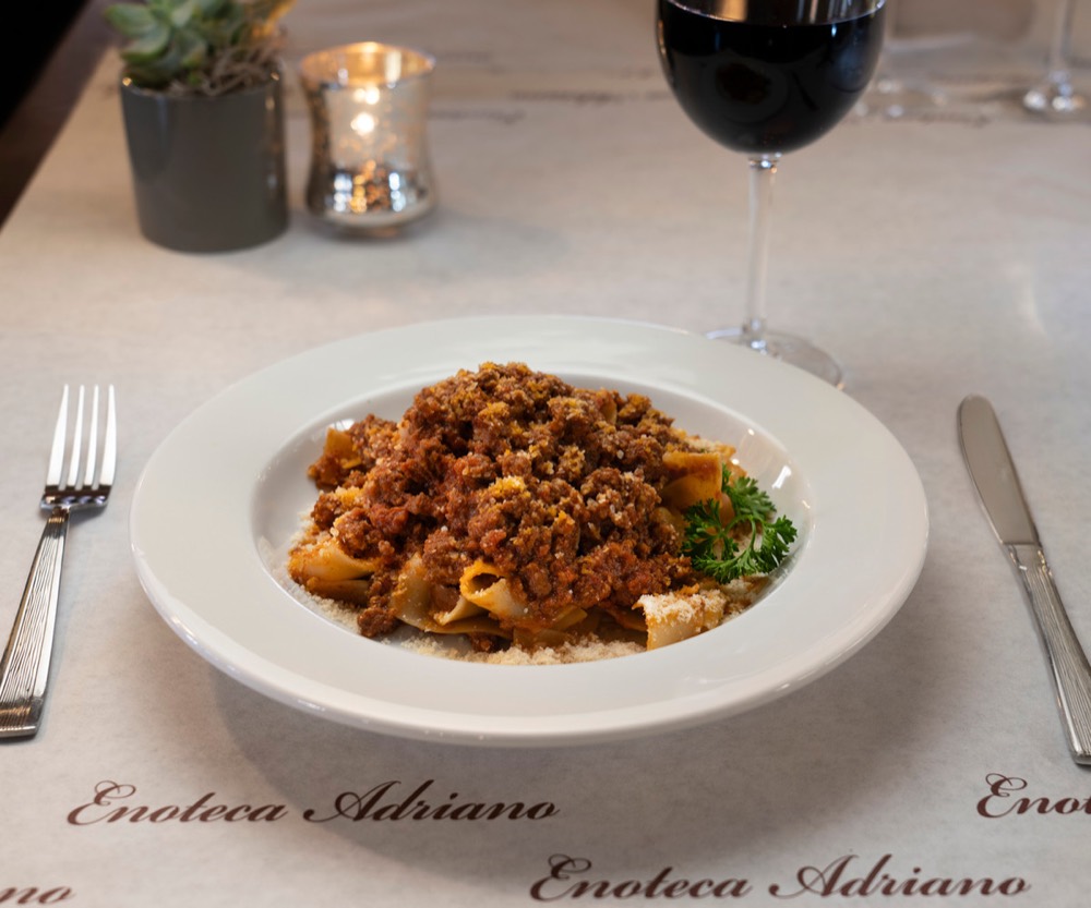 Pasta with ragu and a glass of red wine on a linen tablecloth at Enoteca Adriano