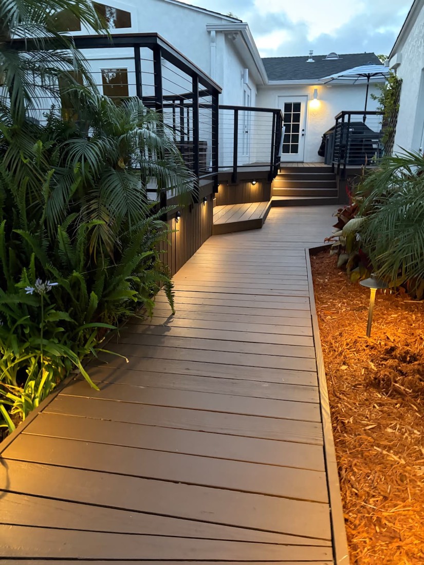 The lit boardwalk running alongside the house up to the deck at dusk