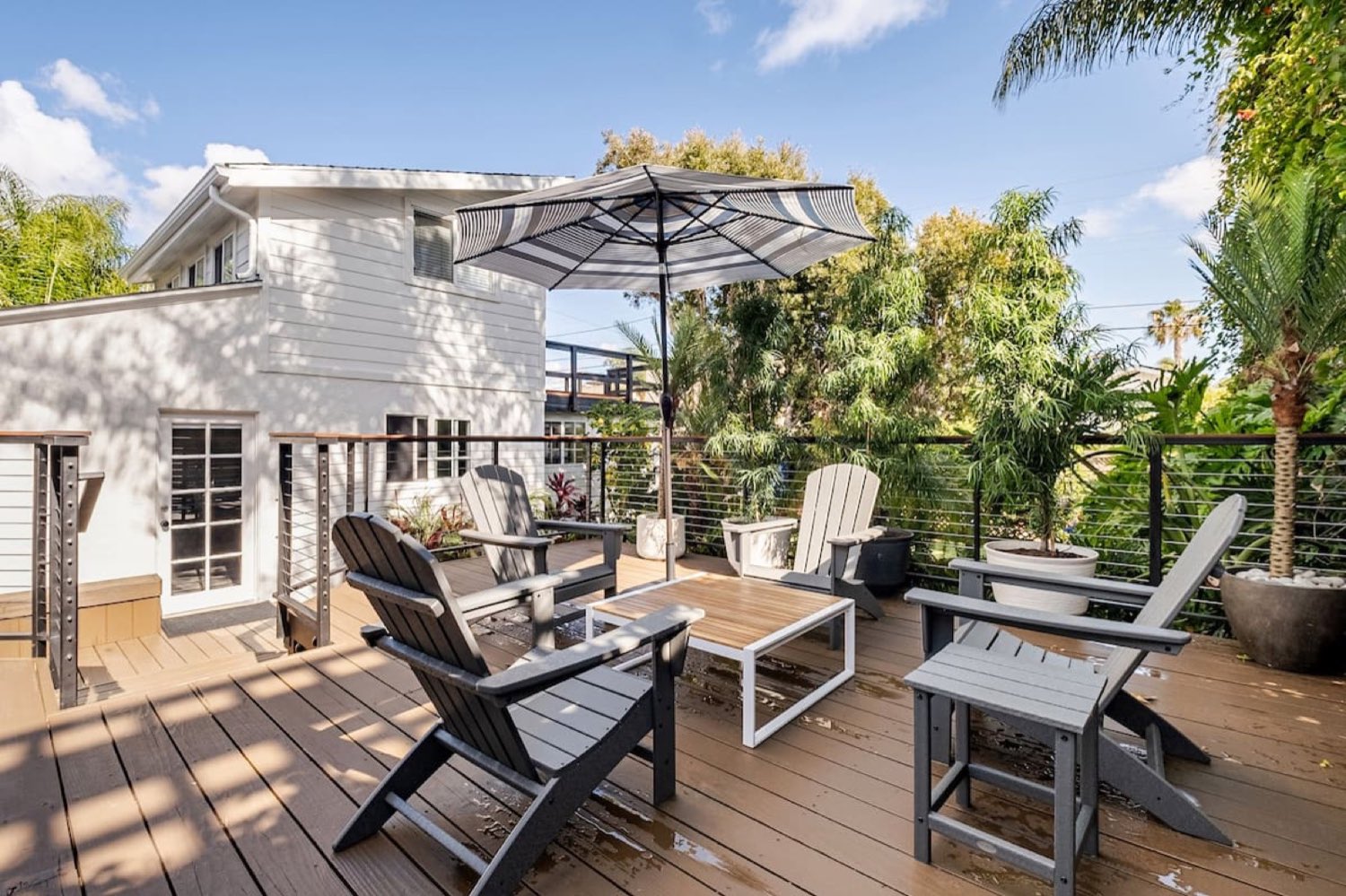 The back deck with Adirondack chairs under a striped umbrella, palms behind
