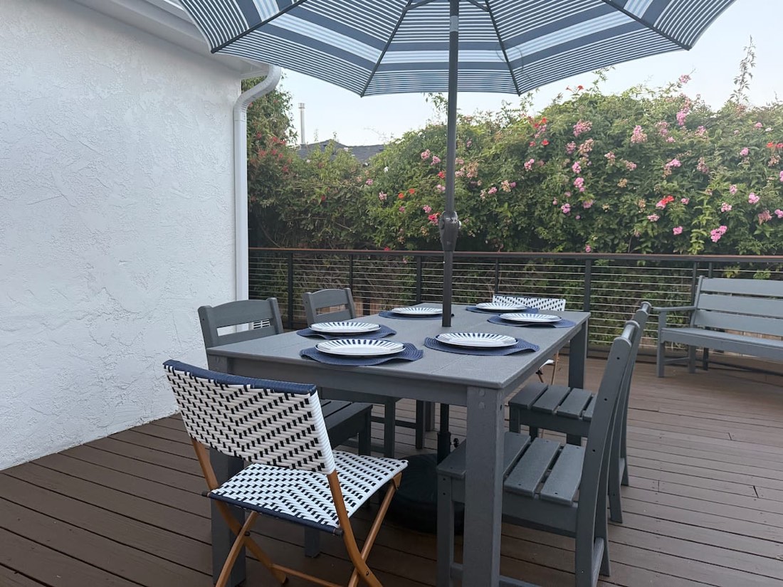 The outdoor dining table on the deck, set for six, with roses along the railing