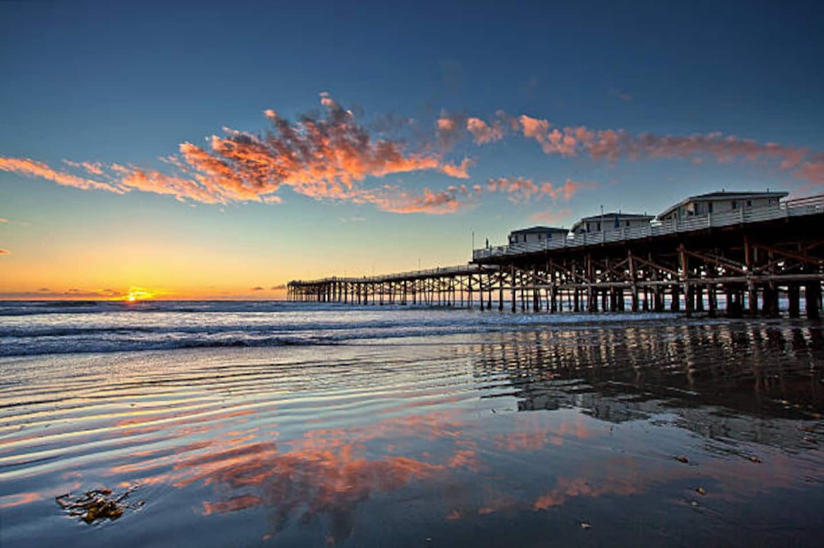 Crystal Pier at sunset with pink cloud reflected on the wet sand